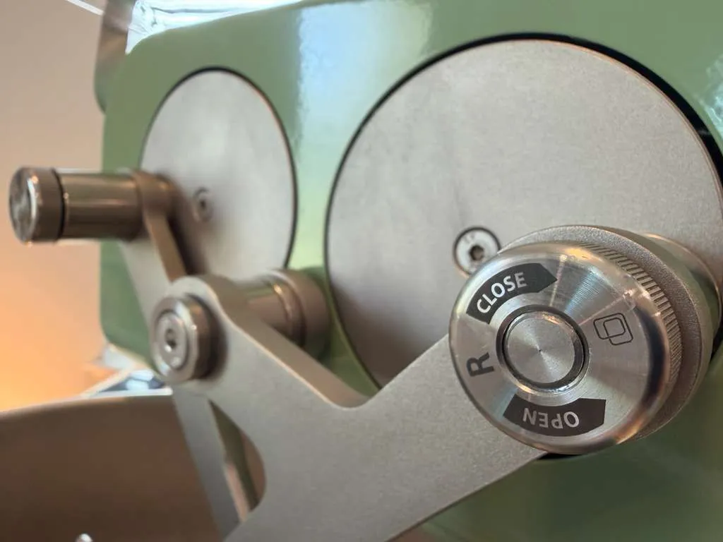Close-up of an arm's release knob, marked Open and Close, on the machine's green head.